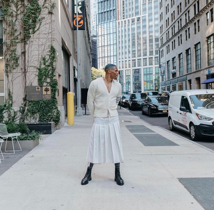 Russel Westbrook poses in a cream sweater, long white skirt and black boots.